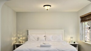 A neatly made bed with white linens and pillows, a bedside table with a lamp, and a window with blinds. - PX002 4 Bedroom Apartment By Senstay (Phoenix)
