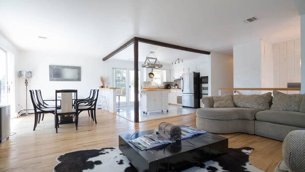 A modern living room with a sofa, a coffee table, and a dining area with chairs. There is a kitchen visible in the background. - SH001 5 Bedroom Holiday home By Senstay (Sagaponack)