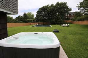 A backyard with a hot tub, a small pool, and lounge chairs.