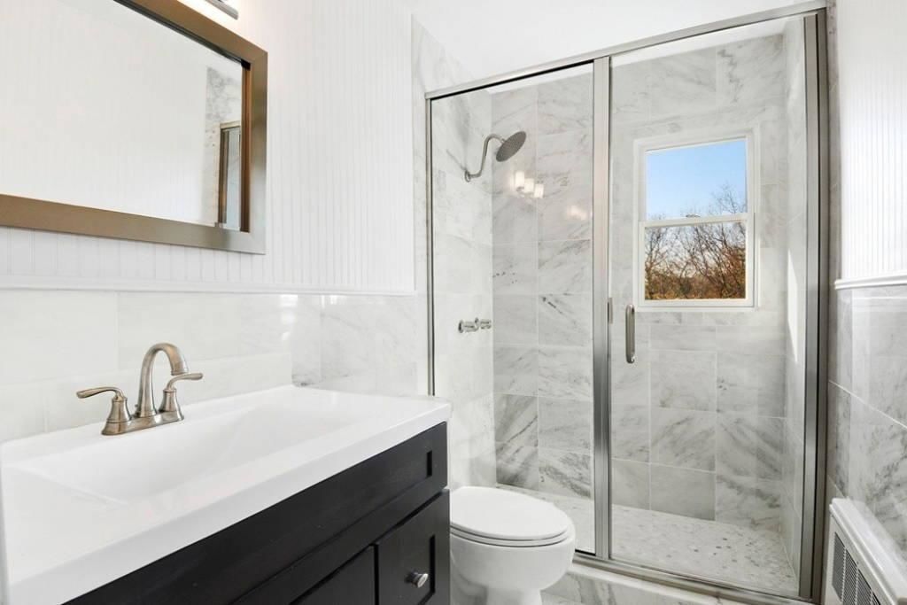 Uma casa de banho moderna com lavatório branco, toucador preto e cabine de duche em vidro.
