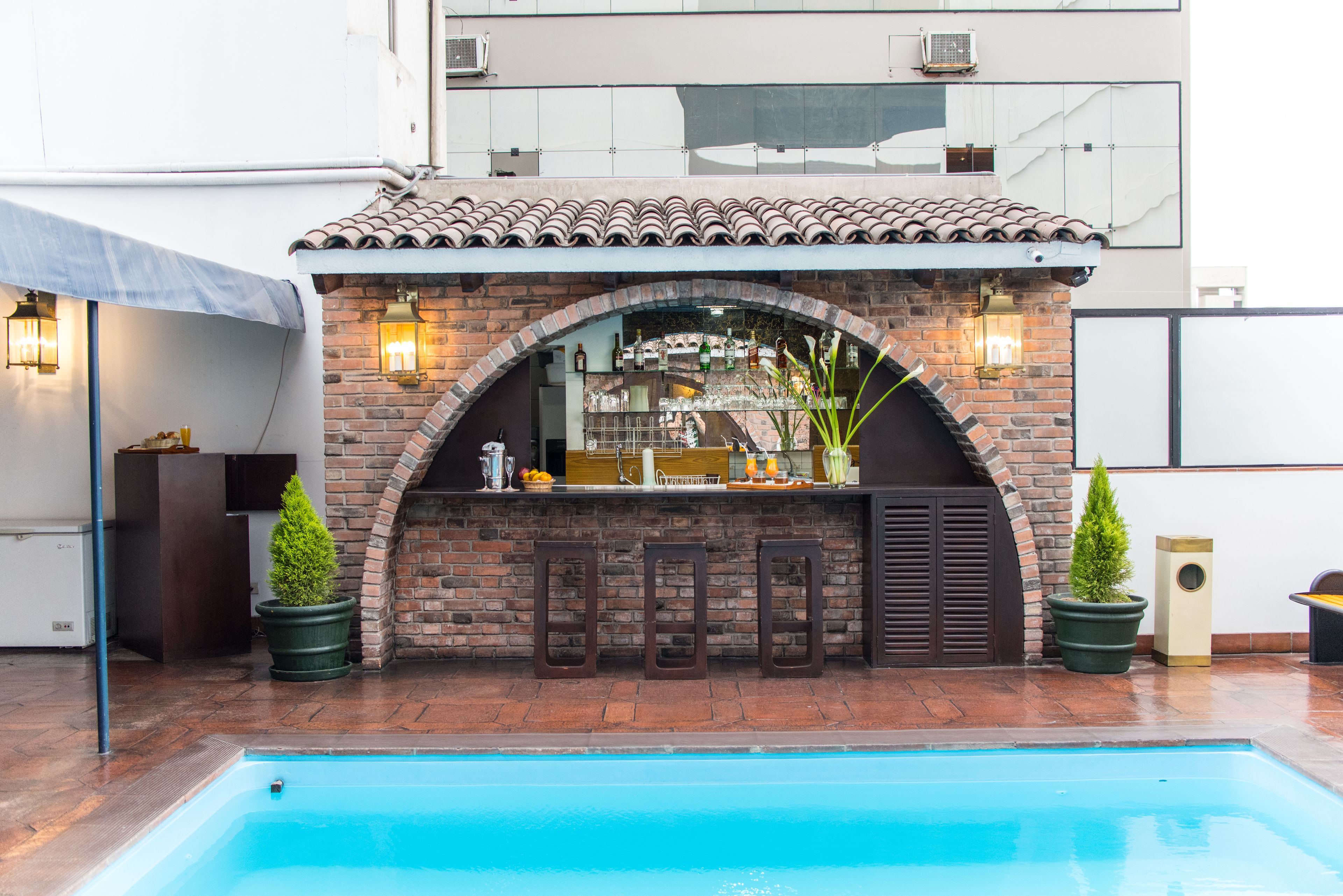 A poolside bar with a brick archway, potted plants, and a tiled roof.