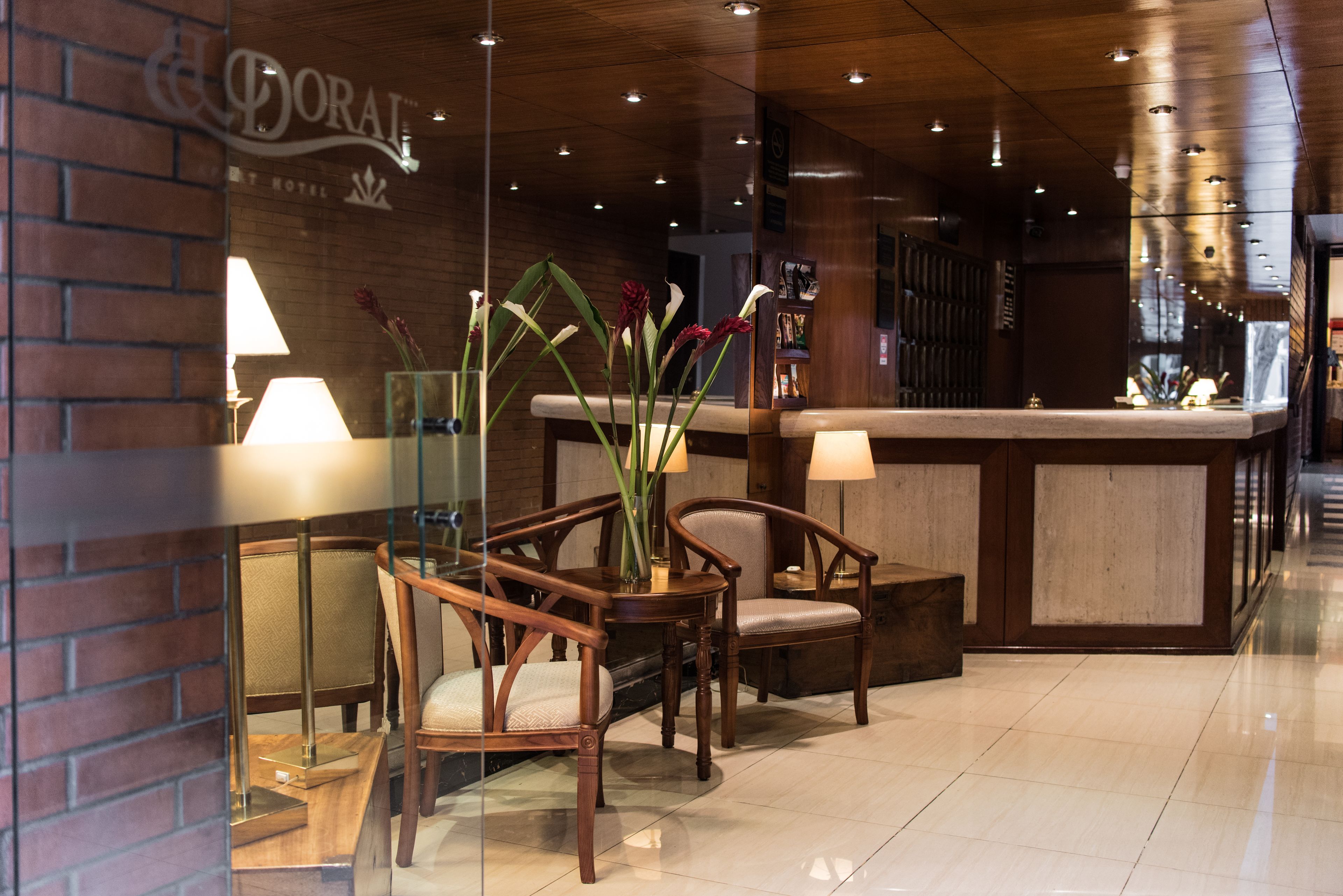 Zona de recepción con mobiliario de madera, un panel de vidrio y una mesa de recepción.
