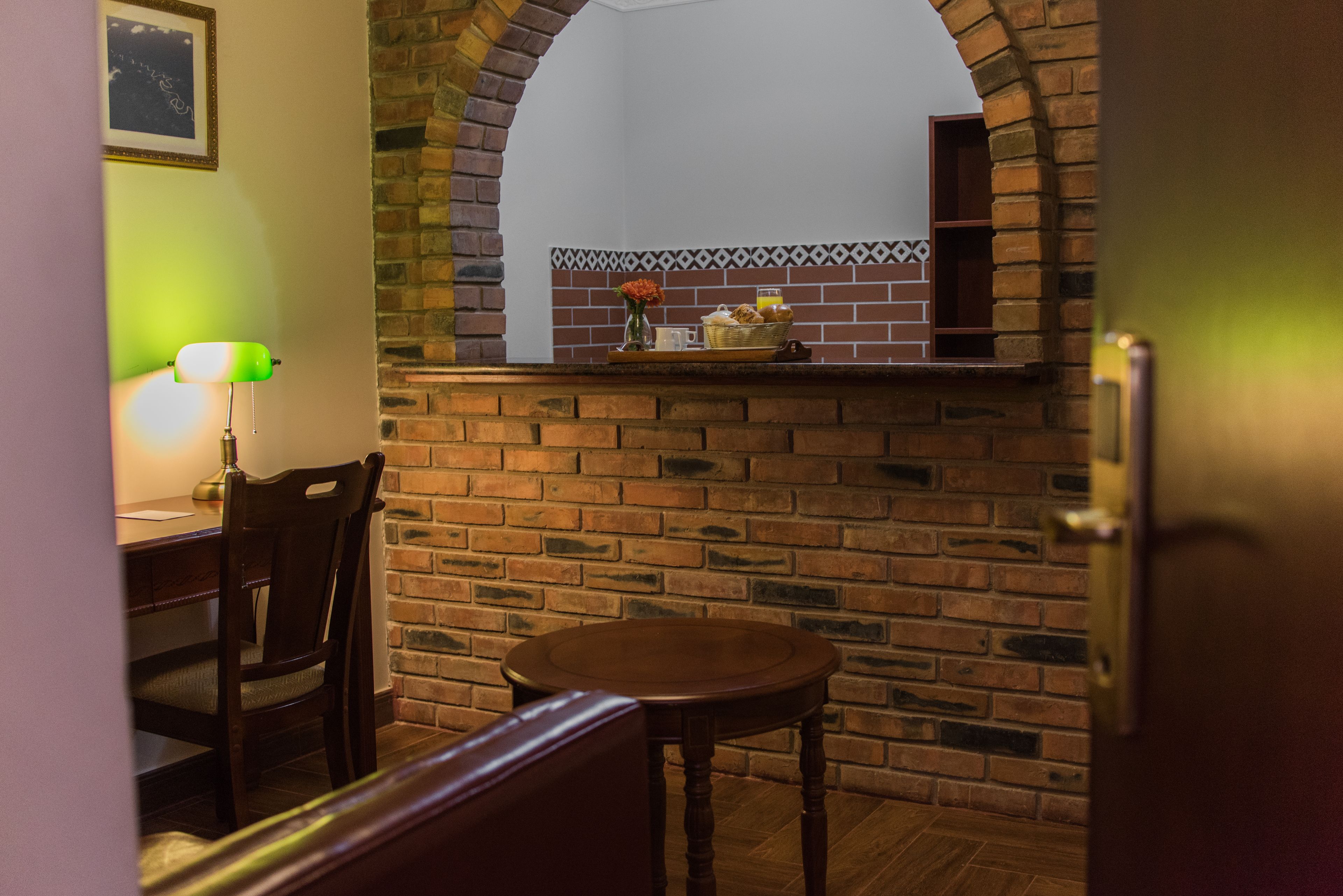 A dining area with a brick wall, a wooden table, a chair, and a lamp.
