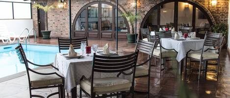An outdoor dining area with a pool, brick walls, and arched doorways.