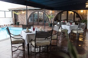 Un área de comedor al aire libre con piscina, paredes de ladrillo y arcos.