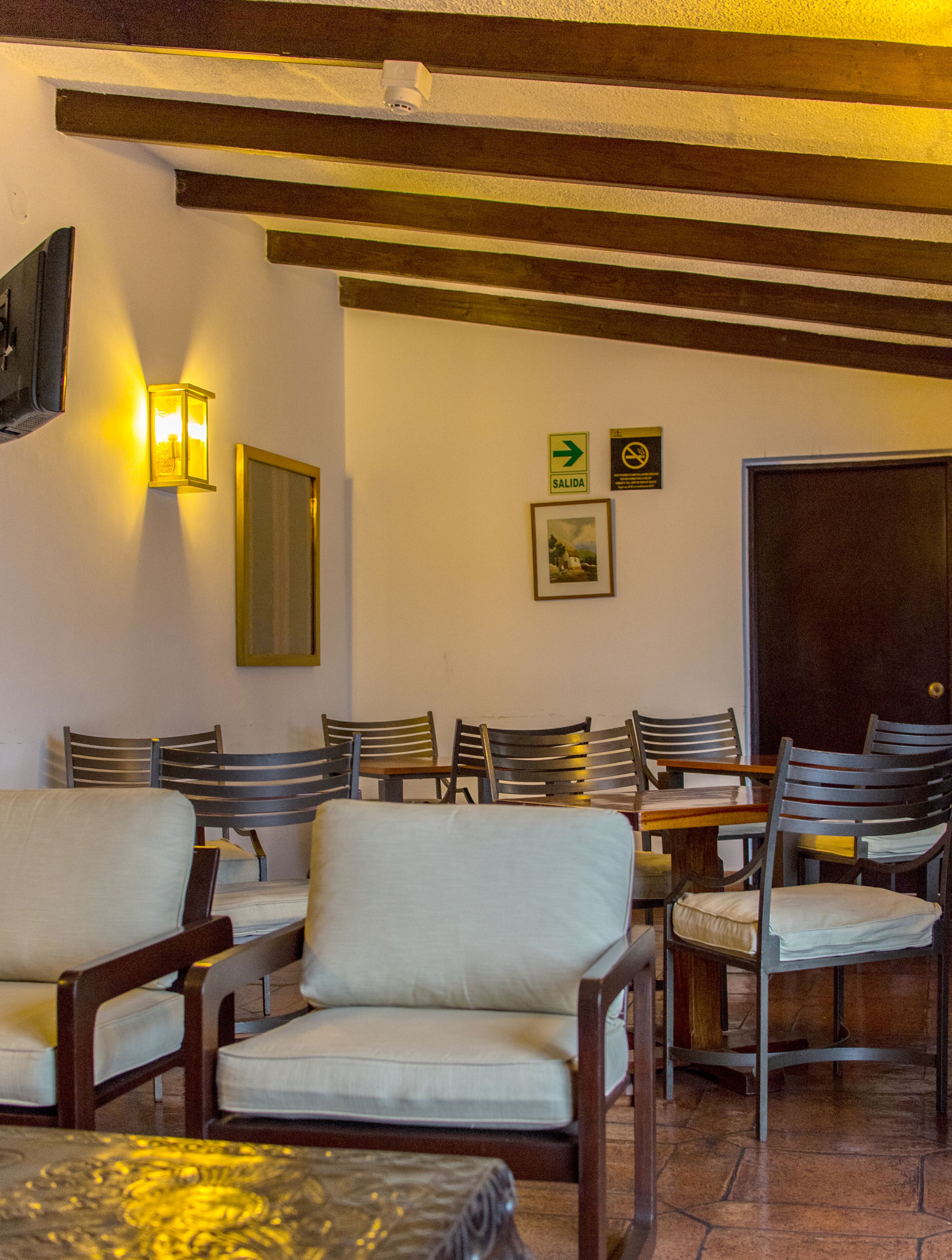 A dining area with wooden chairs and tables, a wall-mounted light, and a door with a sign indicating an exit.