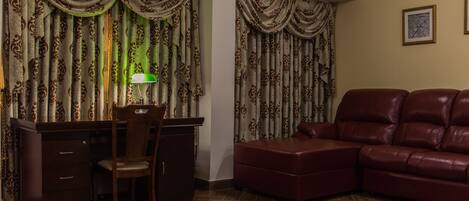 A room with a wooden desk, a leather sofa, and patterned curtains.