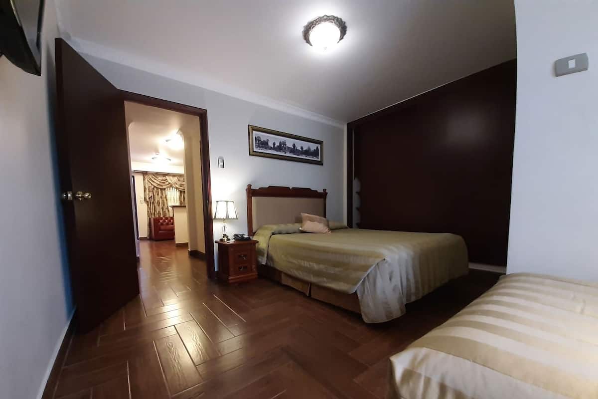 Un dormitorio con suelo de madera, una cama con cabecero, una mesita de noche con lámpara y un cuadro enmarcado en la pared.