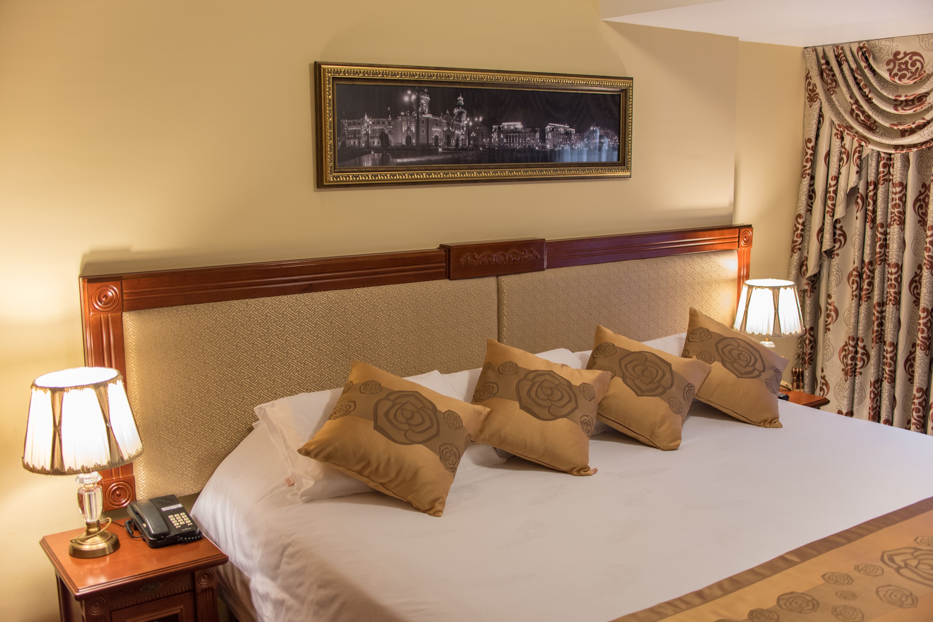 A neatly made bed with patterned pillows, a framed cityscape picture above it, and a telephone on the nightstand.