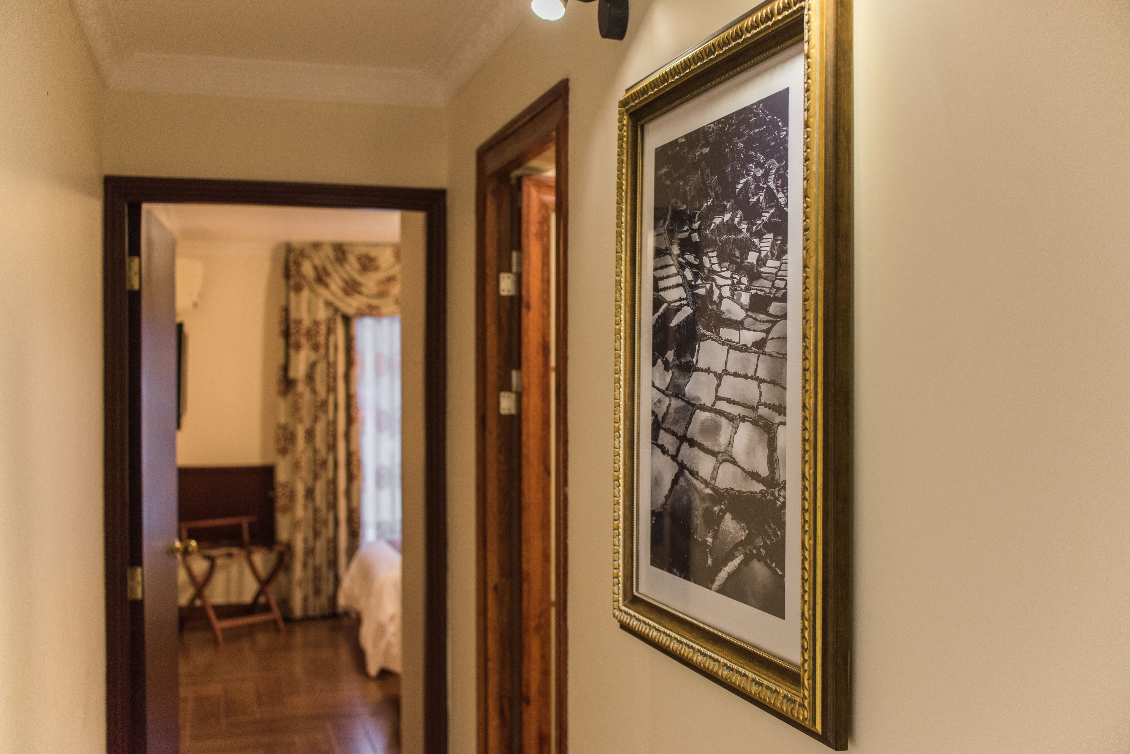 A hallway with a framed black and white photograph on the wall, wooden doors, and a glimpse of a room with a bed and curtains.
