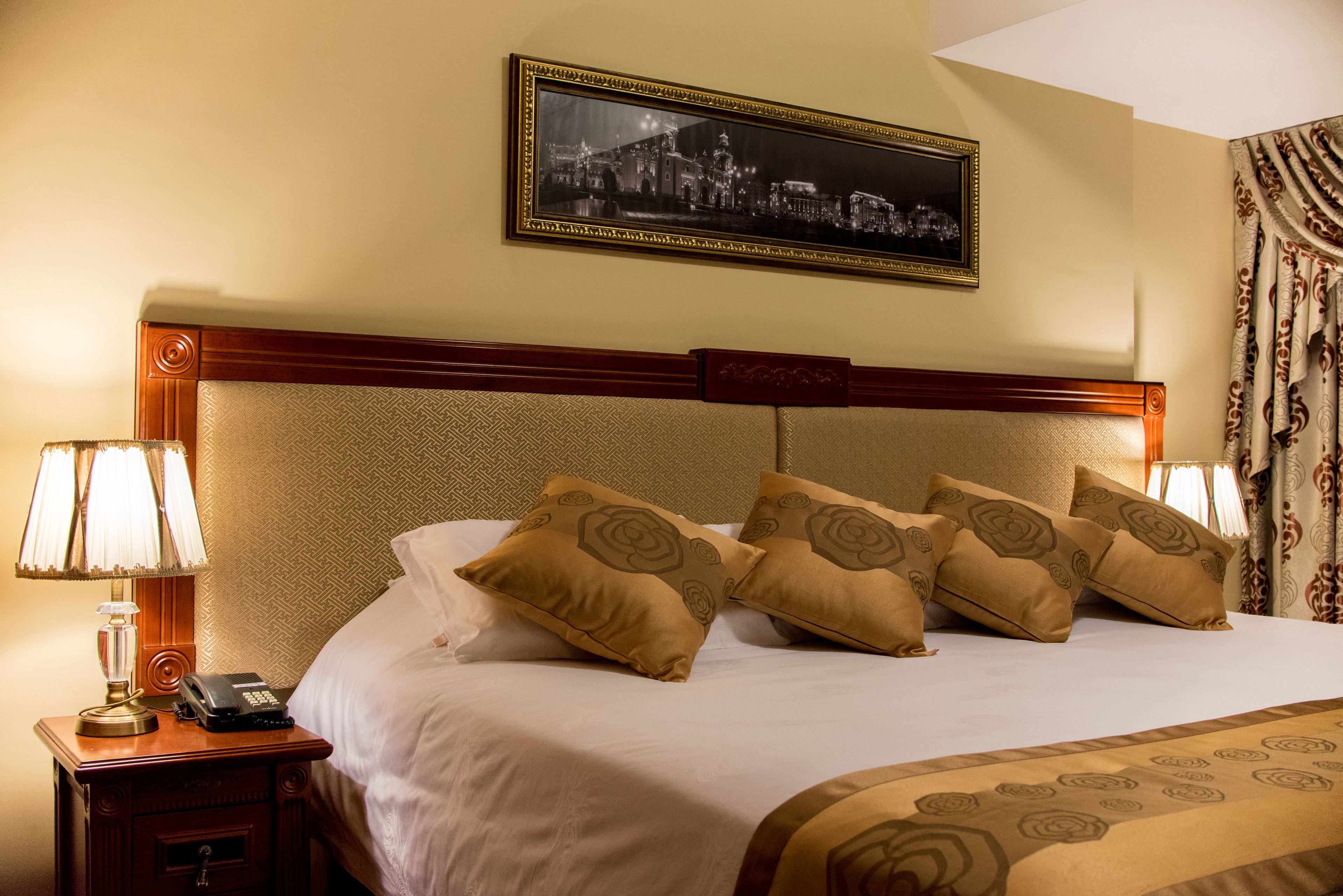 A neatly made bed with a headboard, two bedside lamps, a telephone, and a framed picture on the wall.