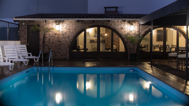 Una piscina con sillas de descanso, un edificio de ladrillo con arcos y un patio cubierto.