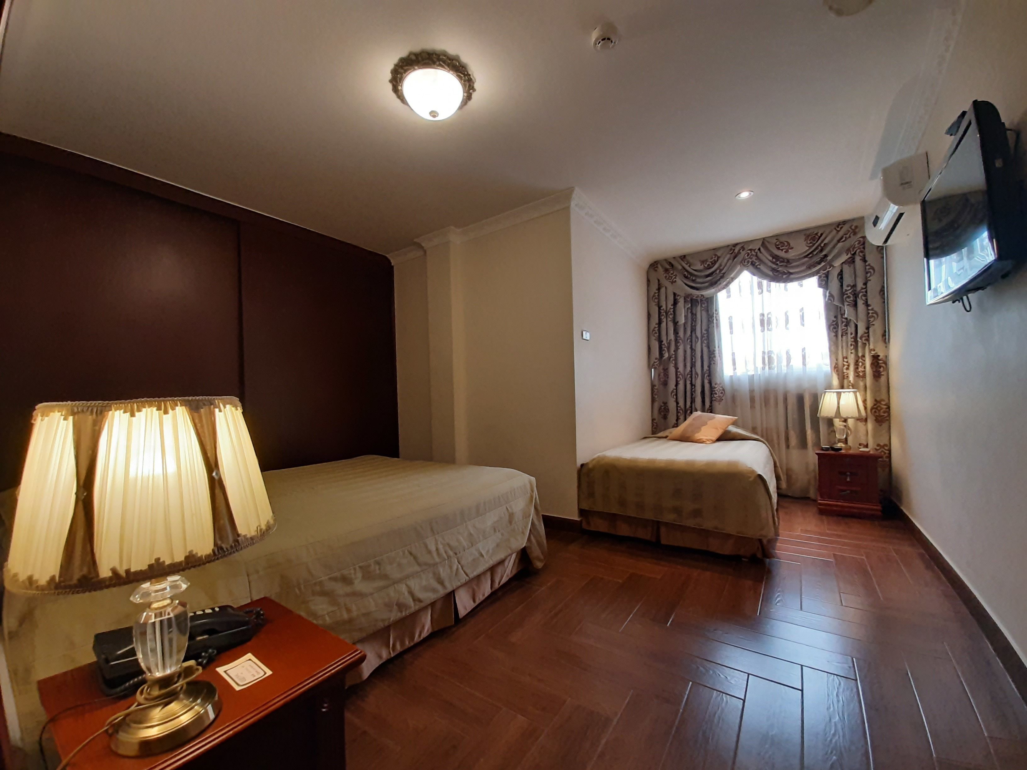A hotel room with a bed, bedside table, lamp, and a television on the wall.