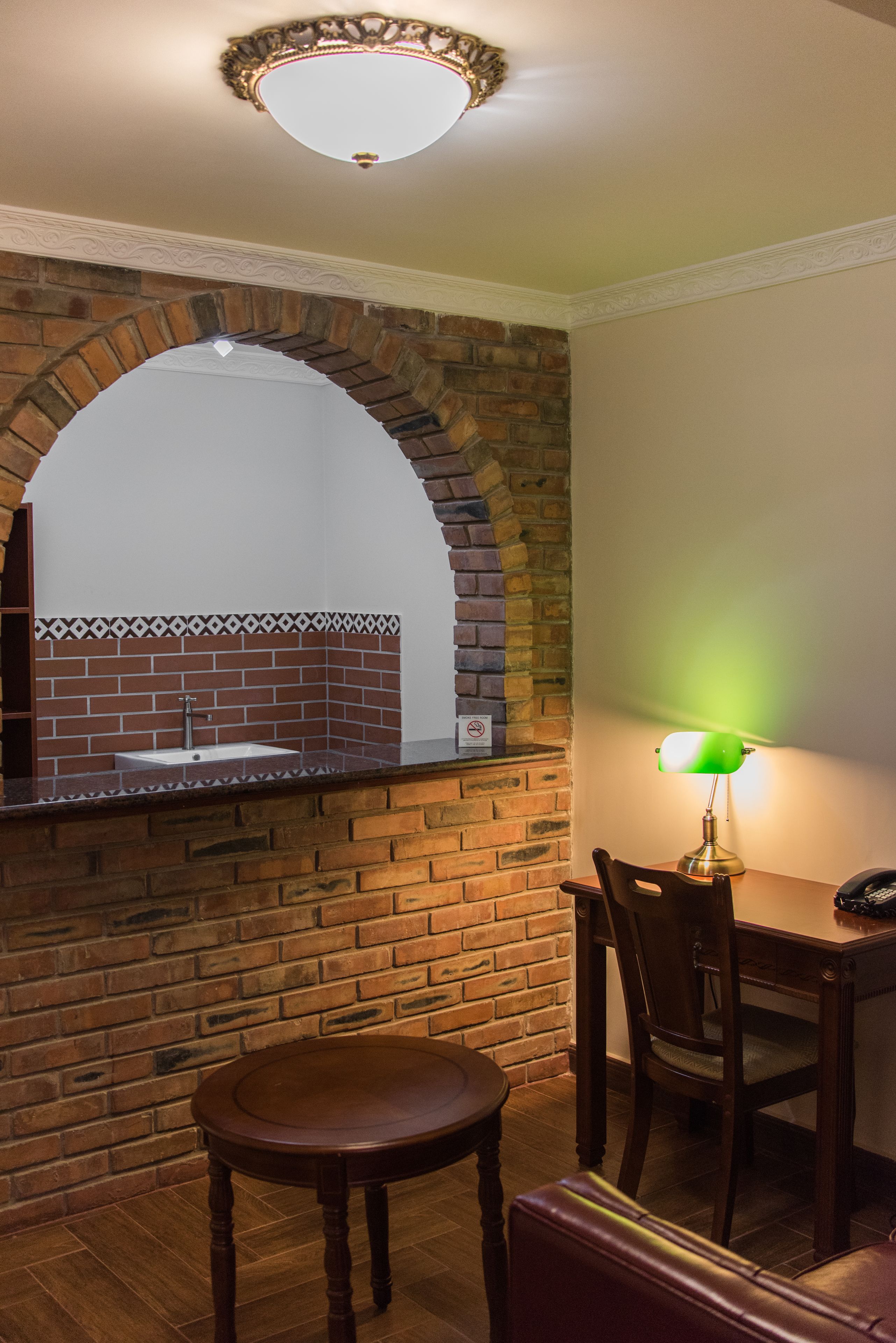 Una habitación con chimenea de ladrillo, una mesa redonda de madera y una lámpara de escritorio verde.