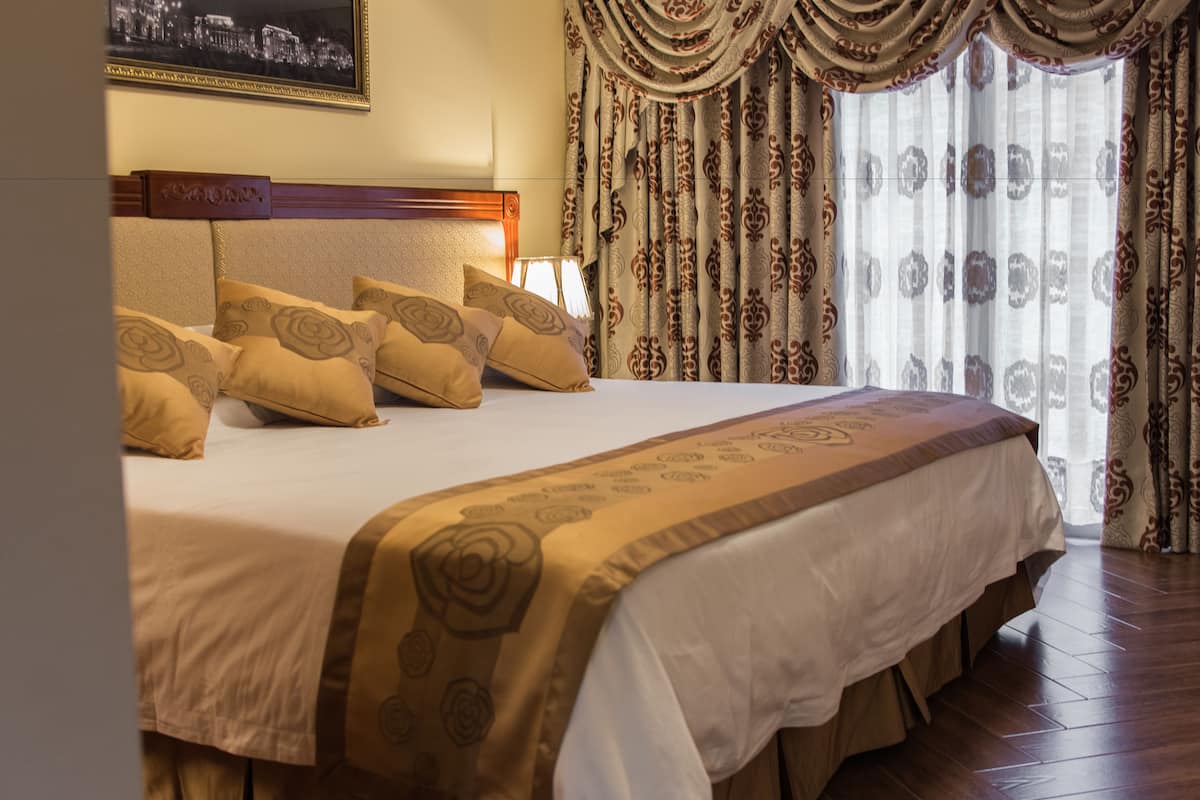Una cama bien hecha con un edredón estampado, un cabecero con panel de madera y cortinas con diseño floral.