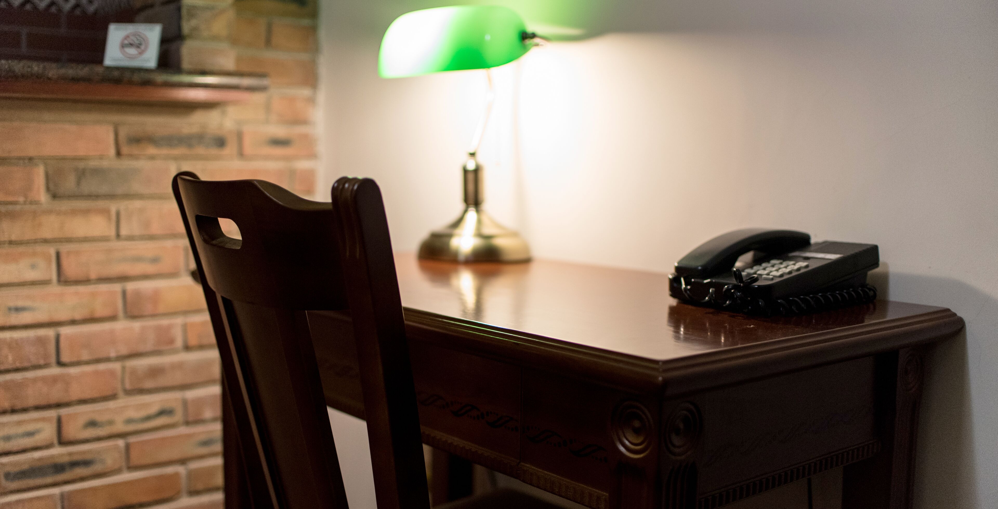 A wooden desk with a telephone and a green desk lamp.