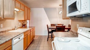 A kitchen with wooden cabinets, a granite countertop, a white dishwasher, a stove, and a dining table with chairs.