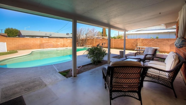 A covered patio with a pool, outdoor furniture, and a brick wall in the background.