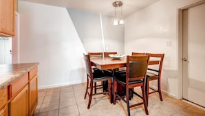 A dining area with a wooden table and chairs, a light fixture above, and a kitchen counter to the left.