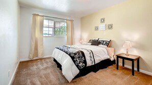 A bedroom with a bed, a window with curtains, a bedside table with a lamp, and wall decorations.