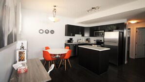 A compact kitchen with dark cabinets, a central island, and a dining area with orange chairs. - Elegant Suite (Saskatoon)