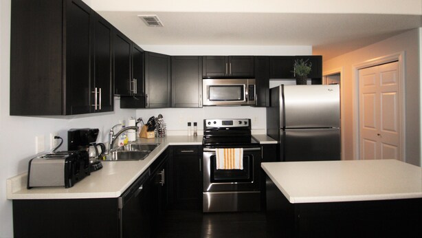 A modern kitchen with dark cabinets, stainless steel appliances, and a white countertop. - Elegant Suite (Saskatoon)