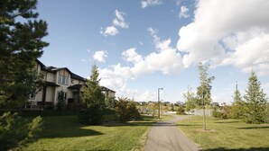 A residential area with a paved pathway leading to a house with a dark roof and multiple windows. - Elegant Suite (Saskatoon)