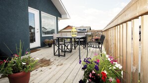 A wooden deck with outdoor furniture, a potted plant, and a building with a dark exterior. - Elegant Suite (Saskatoon)