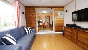 Une pièce avec un plancher en bois, un canapé bleu orné de coussins à rayures, un téléviseur fixé au mur et un meuble en bois.