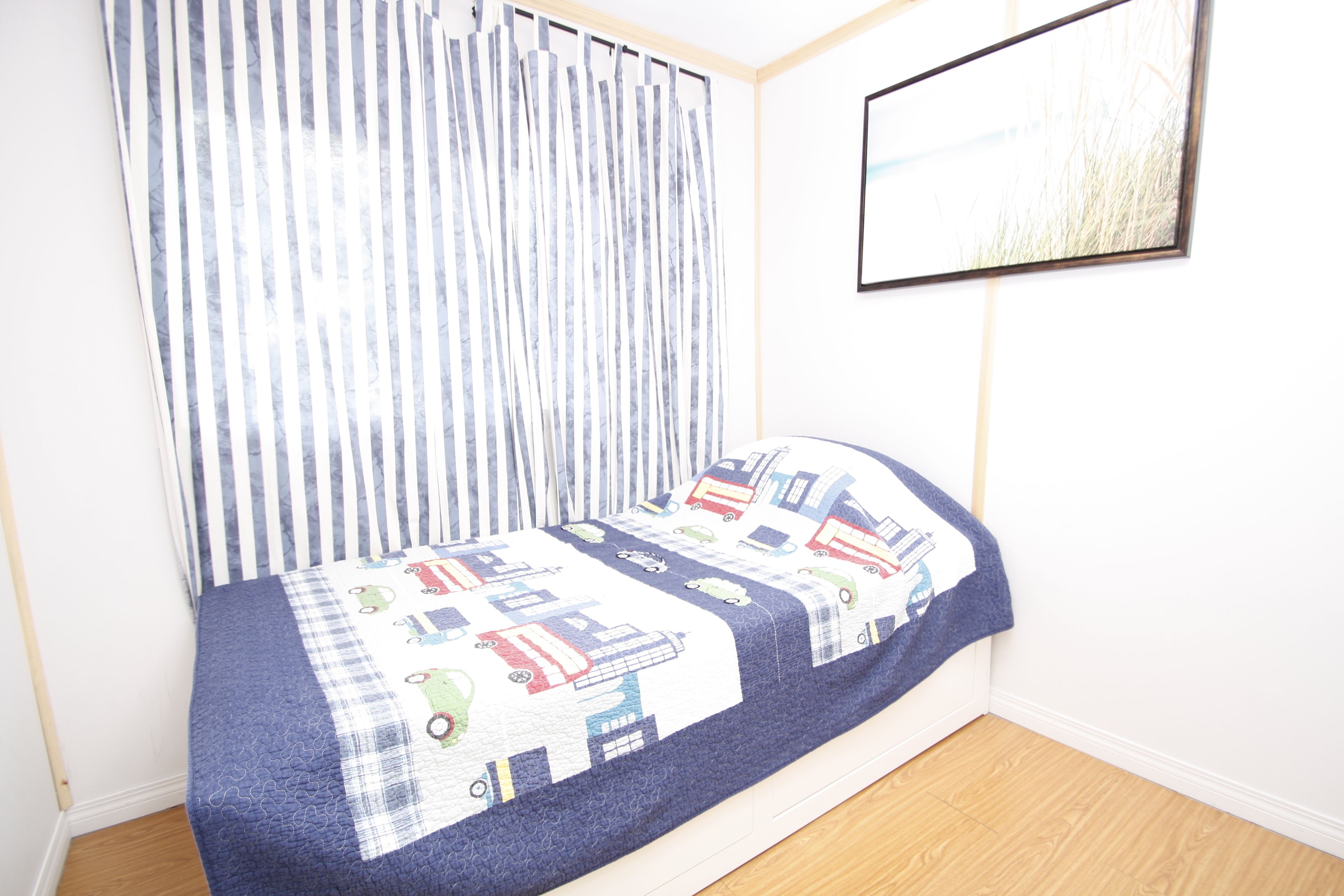 Une petite chambre à coucher avec un lit, une fenêtre avec des rideaux et un tableau encadré accroché au mur.