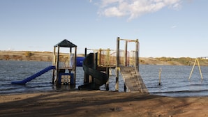 Un terrain de jeux avec un toboggan et des structures d’escalade, situé près d’une étendue d’eau.