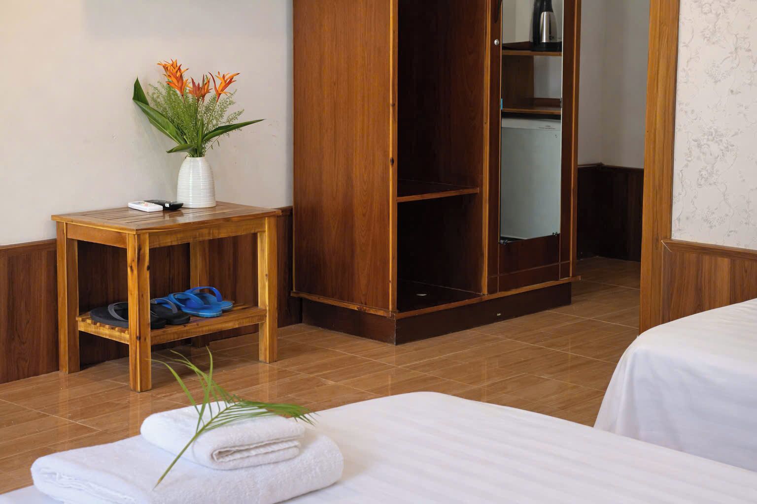 Une chambre d’hôtel avec une table en bois, un vase rempli de fleurs, une armoire et un lit avec une serviette.