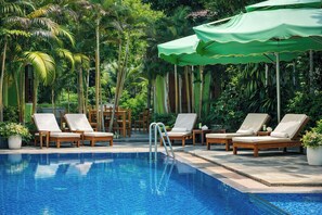 Zona de piscina con sillas de descanso y sombrillas, rodeada de abundante vegetación.