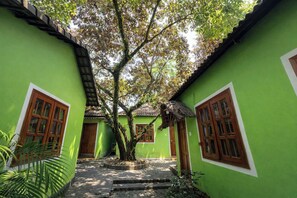 A green building with a central tree, a thatched roof, and a paved pathway.