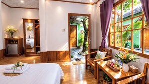 A hotel room with a bed, wooden furniture, a dining table with a fruit basket, and a view of a garden through large windows. - FORTUNE HOTEL 2 LUCKY STAY Phu Quoc (Phu Quoc)