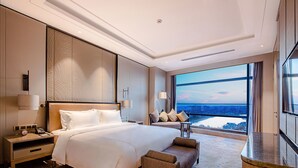 A modern hotel room with a large bed, a nightstand, a desk, and a view of the cityscape through large windows. - Golden Eagle Summit Hotel Nanjing China (Nanjing)