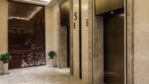 A modern elevator with a metallic finish, number 5, in a lobby with marble flooring and decorative panels. - Golden Eagle Summit Hotel Nanjing China (Nanjing)