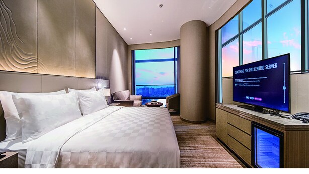 A modern hotel room with a large bed, a desk, a TV, and a city view. - Golden Eagle Summit Hotel Nanjing China (Nanjing)