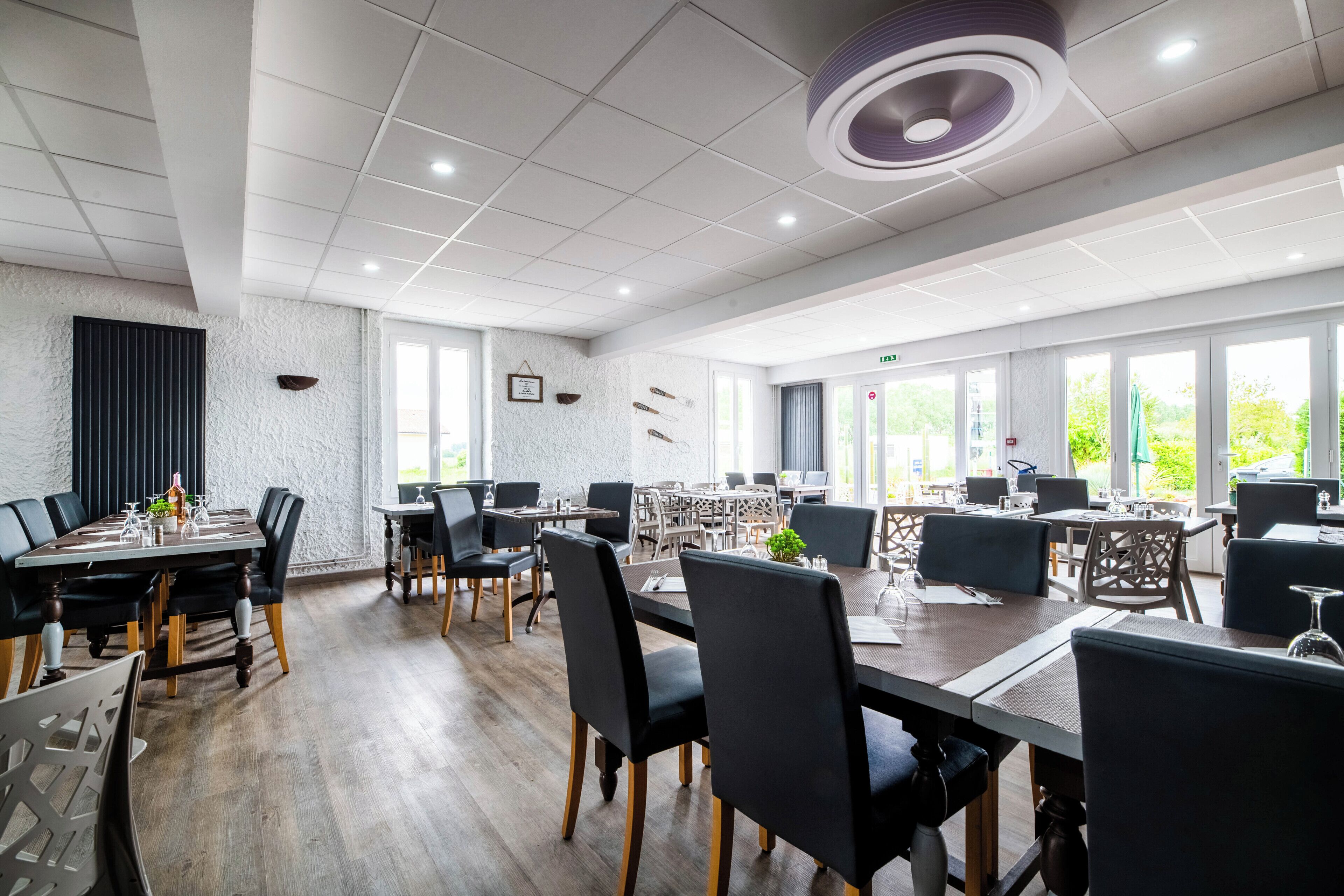 A spacious conference room with multiple tables and chairs, large windows, and a modern ceiling design.