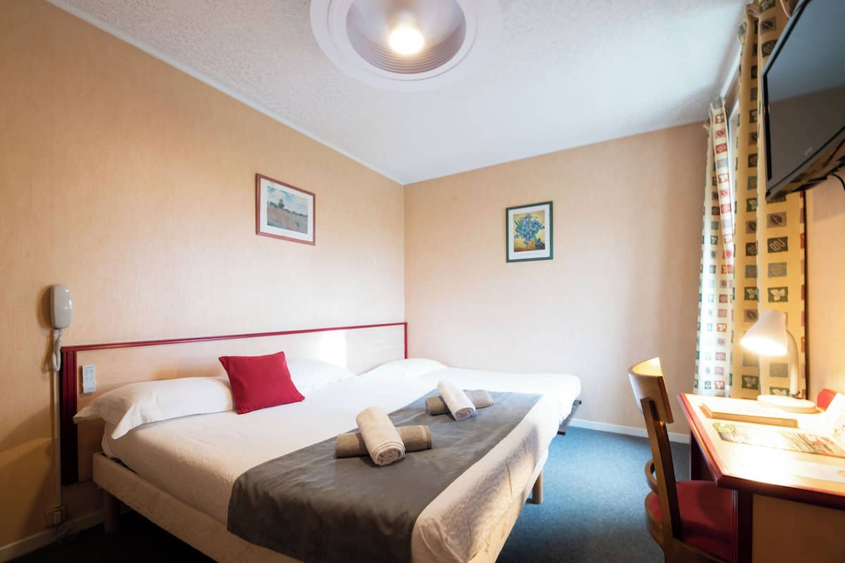 Une chambre d’hôtel avec deux lits, un bureau, une chaise et un téléviseur.
