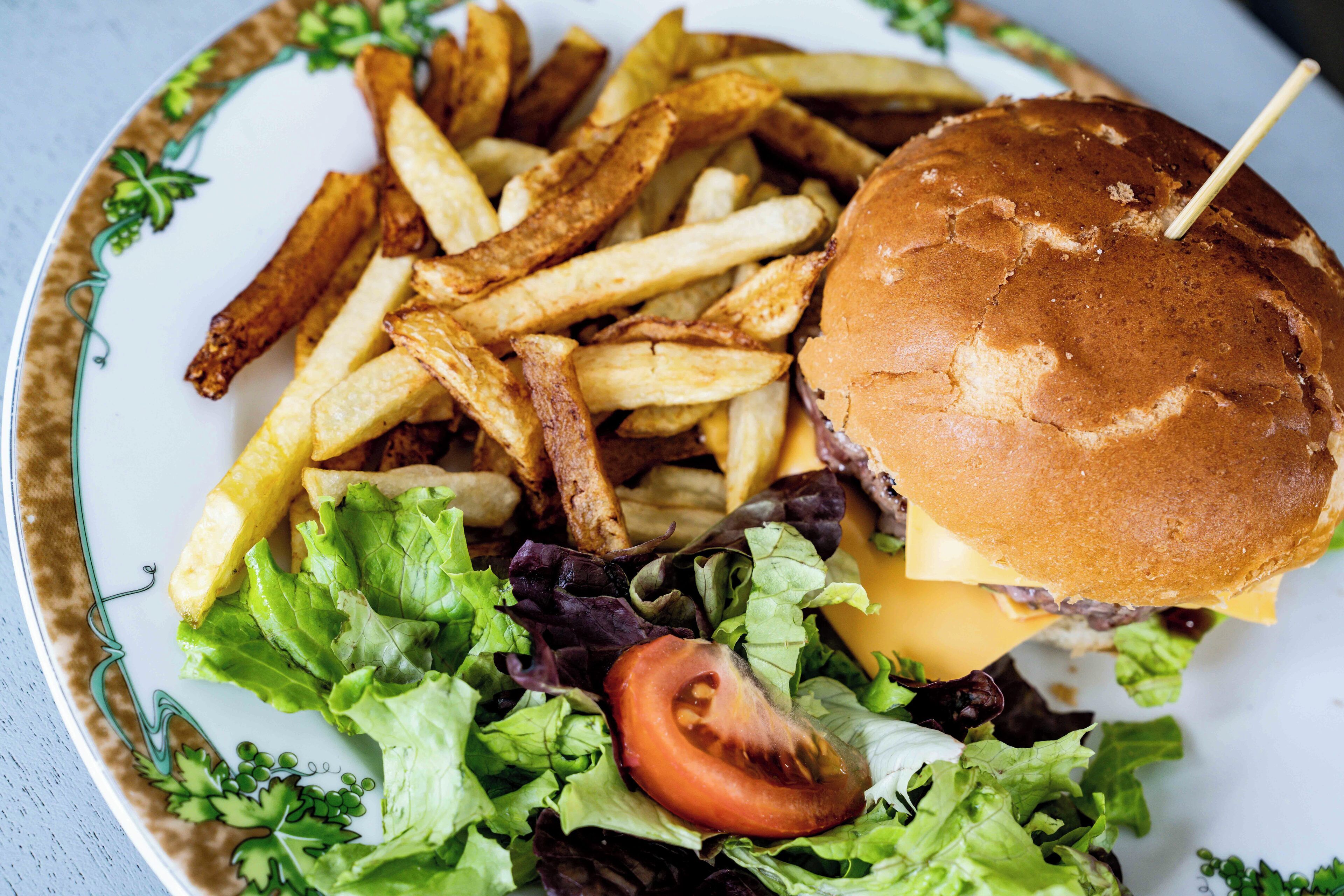 A plate with a burger, fries, lettuce, and a tomato.