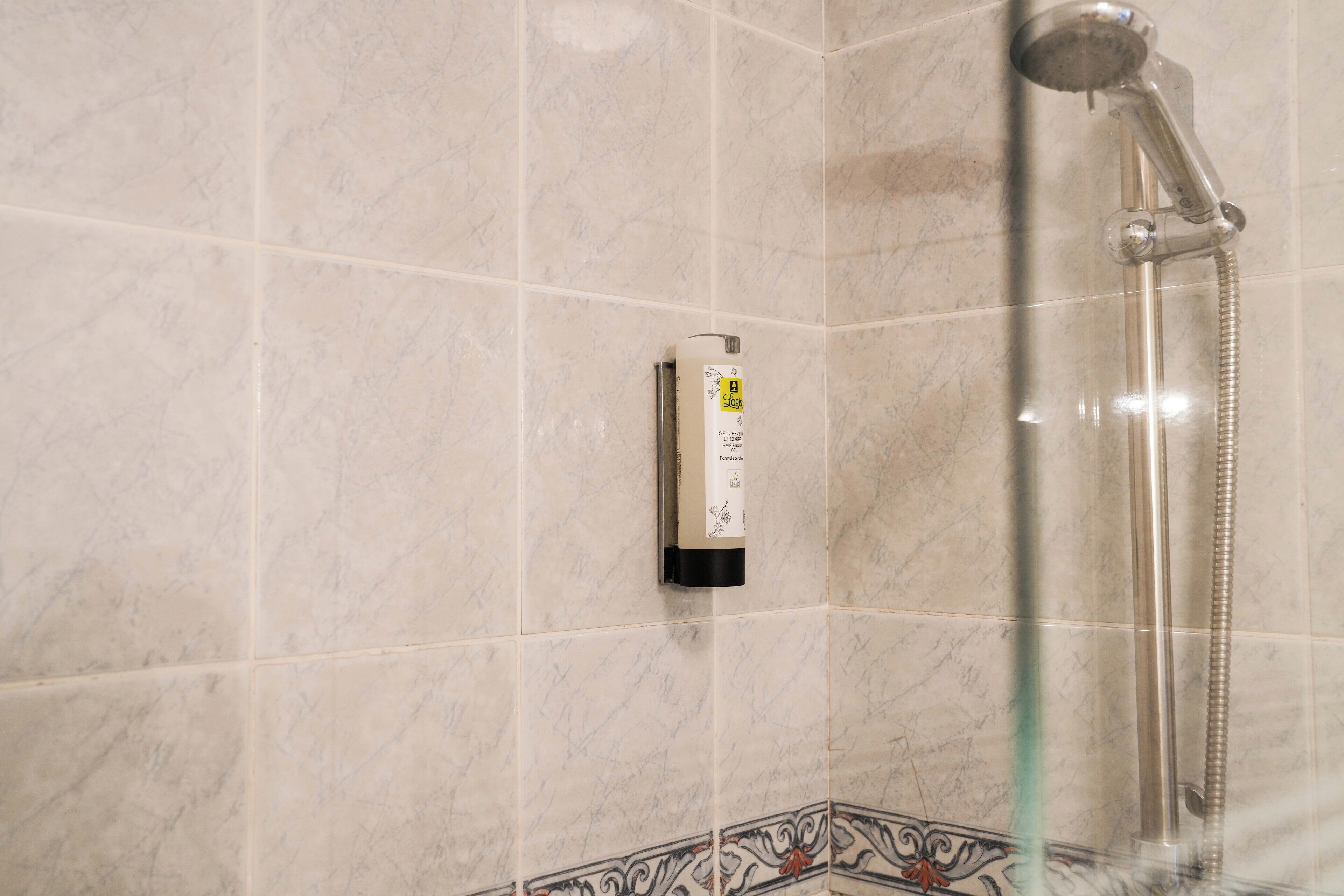 Une salle de bain carrelée de marbre, dotée d’une douchette à main et d’un distributeur de savon.
