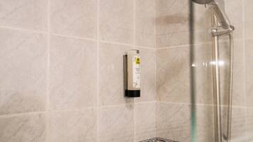 Une salle de bain carrelée de marbre, dotée d’une douchette à main et d’un distributeur de savon.