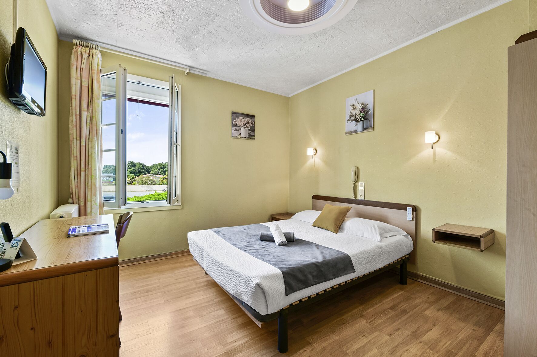 A bedroom with a bed, a desk, a window with curtains, and wall-mounted lights.