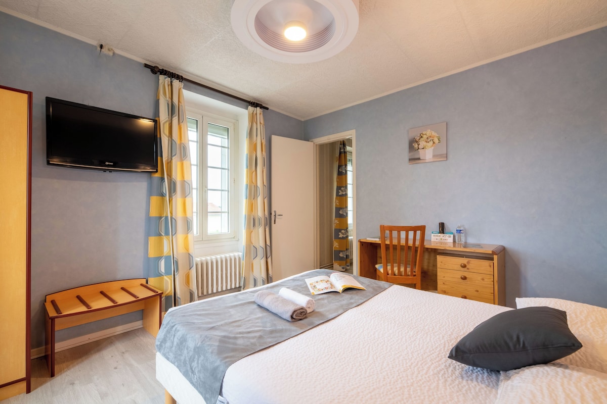 A bedroom with a bed, a desk, a chair, a television, and a window with curtains.