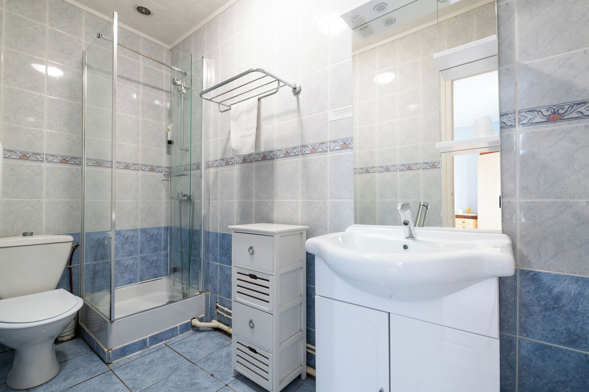 A bathroom with a glass shower enclosure, a toilet, a sink, and a cabinet.