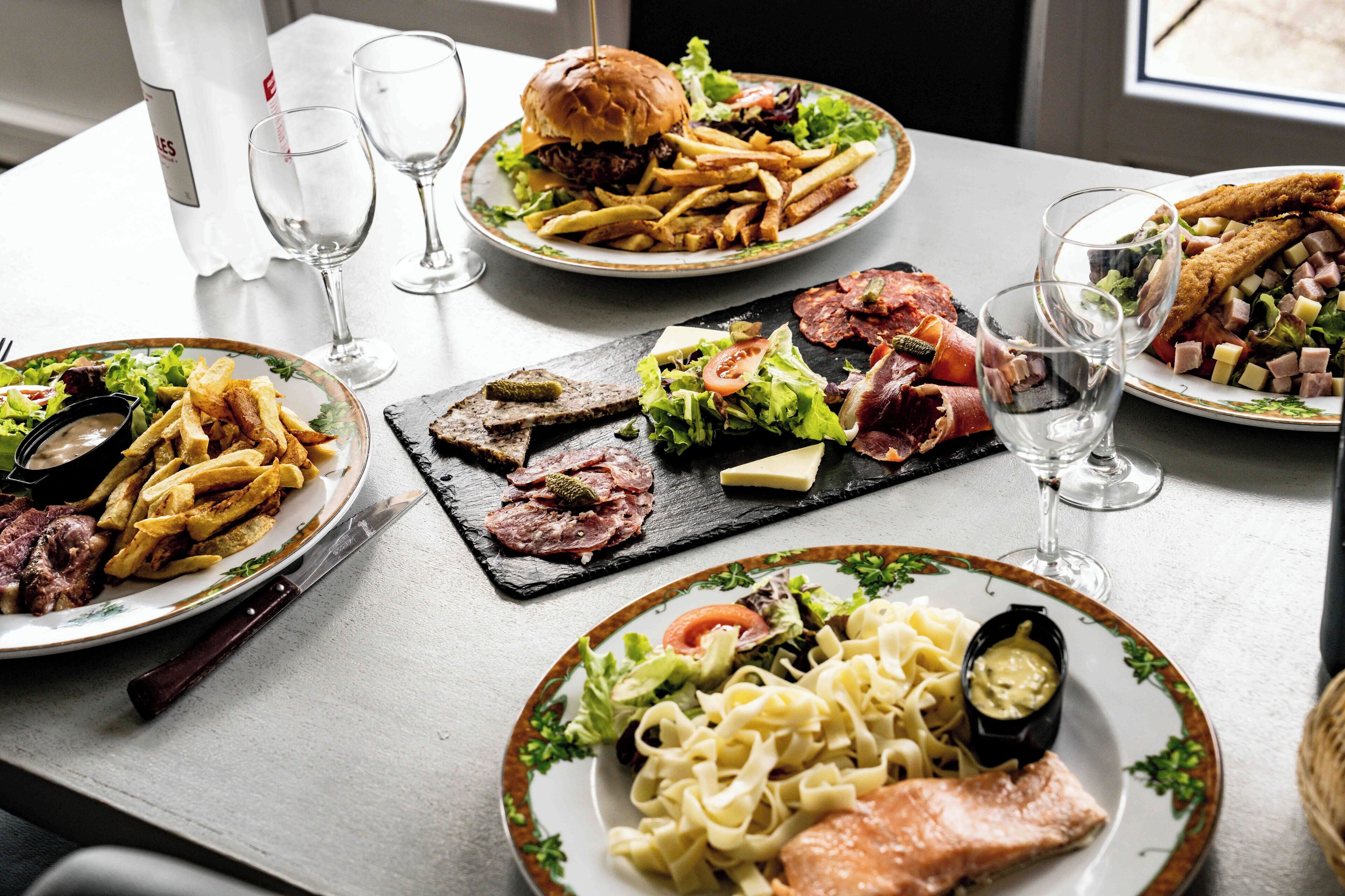 Una mesa con varios platos, incluyendo una hamburguesa, papas fritas, ensalada y pasta.