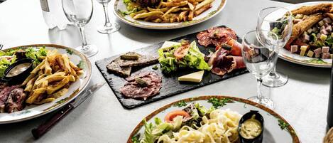 Una mesa con varios platos, incluyendo una hamburguesa, papas fritas, ensalada y pasta.