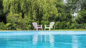 Een zwembad met twee Adirondack-stoelen, omgeven door weelderige begroeiing.