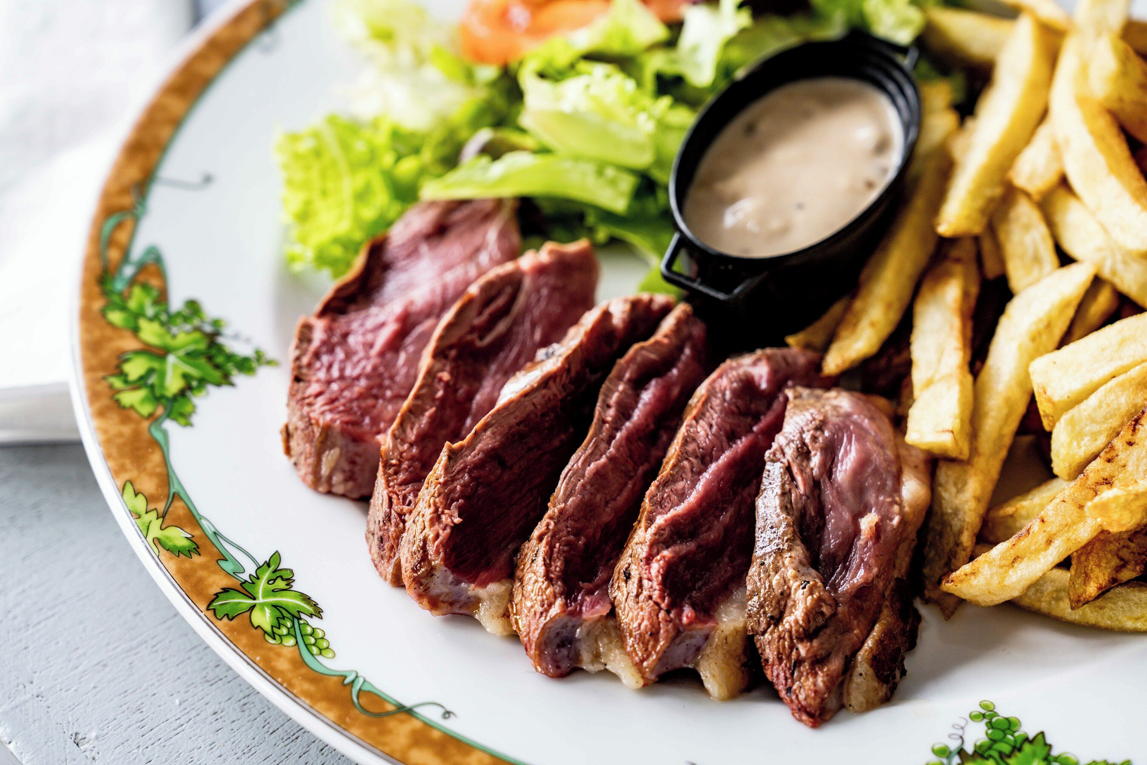 A plate with sliced meat, fries, and a small bowl of sauce.